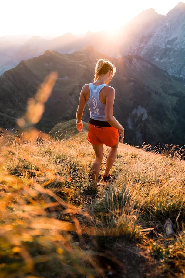 Nainen kävelee vuorta alas oranseissa shortseissa ja sinisessä Swix urheilupaidassa. 
